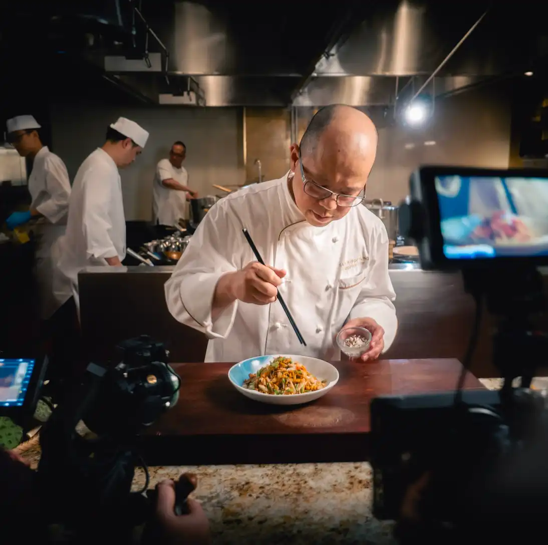 Chef seasoning a prepared dish on the countertop in a professional kitchen.