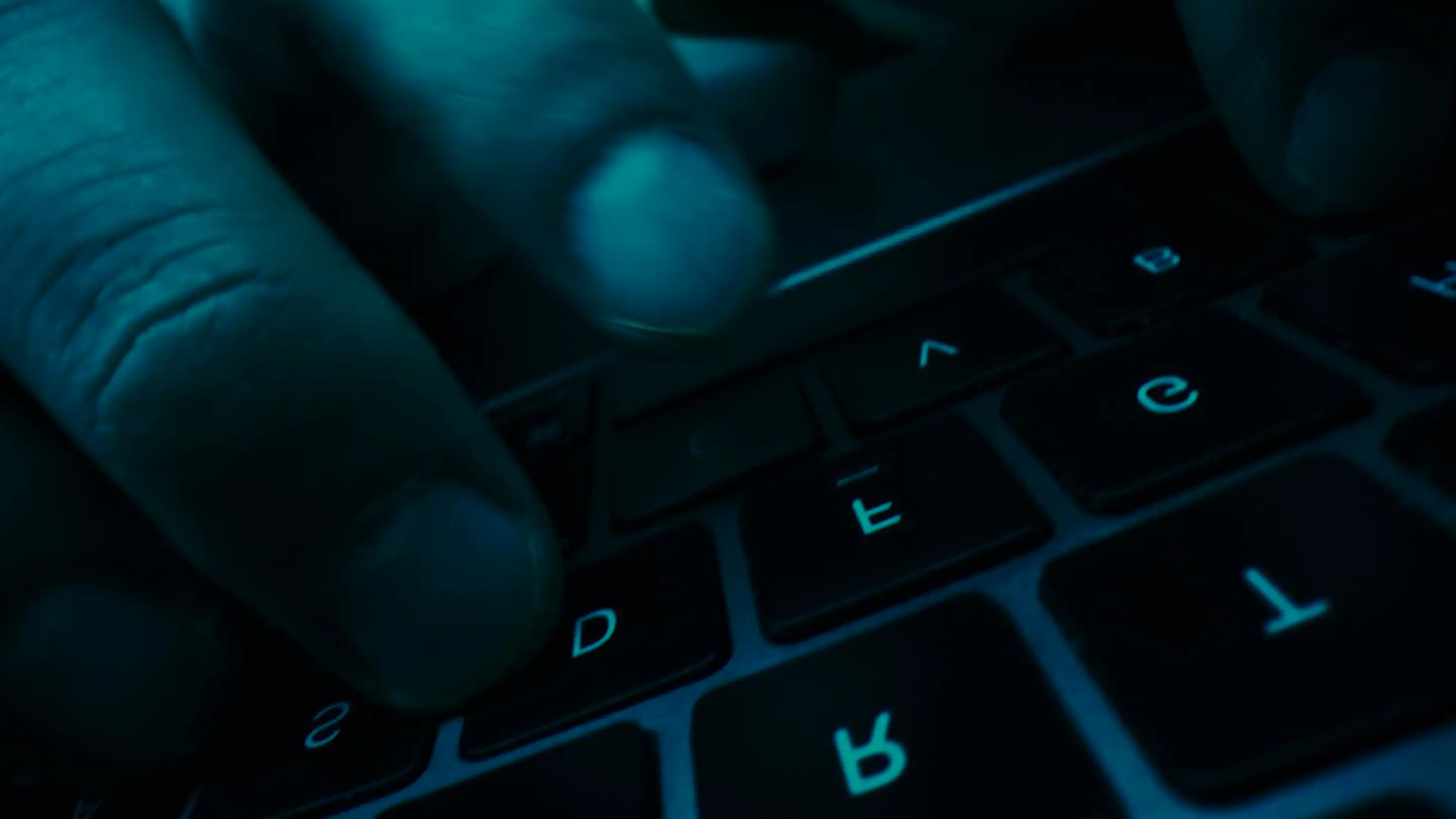 Close-up of hands typing on a backlit keyboard in low light.
