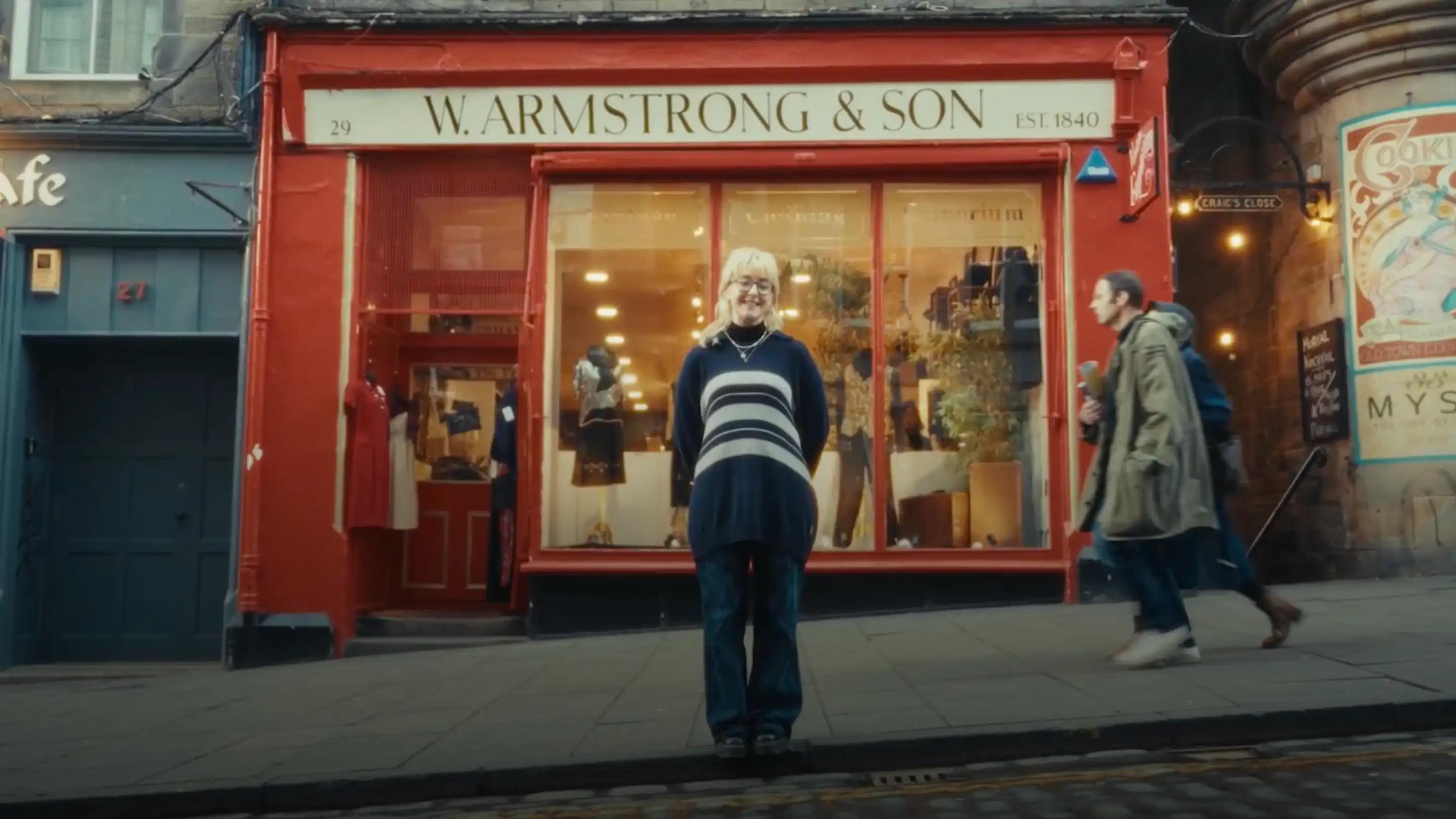 A smiling woman standing in front of W. Armstrong & Son clothing store on a city sidewalk.