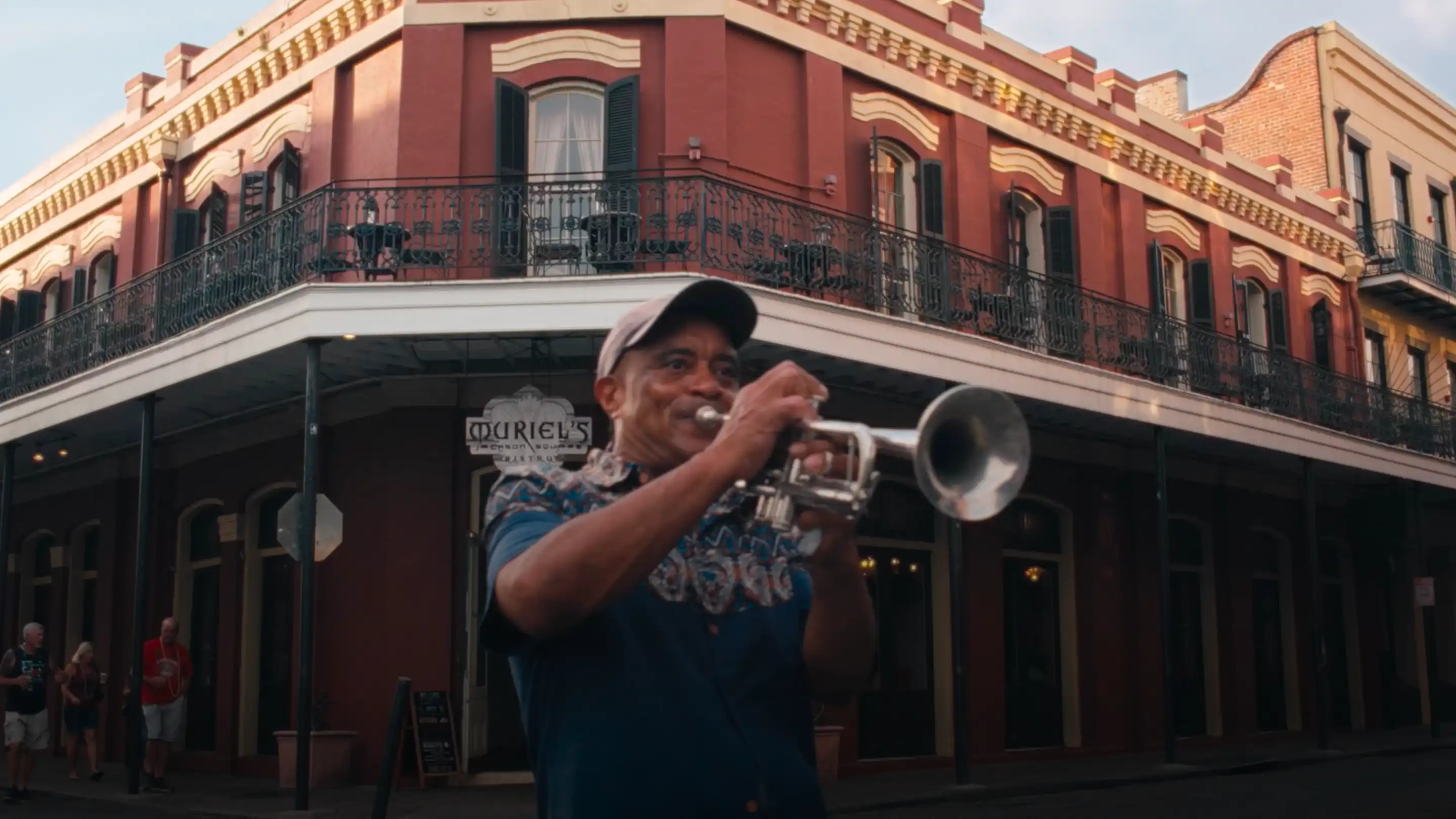 Man playing trumpet on street corner in front of a red brick building.