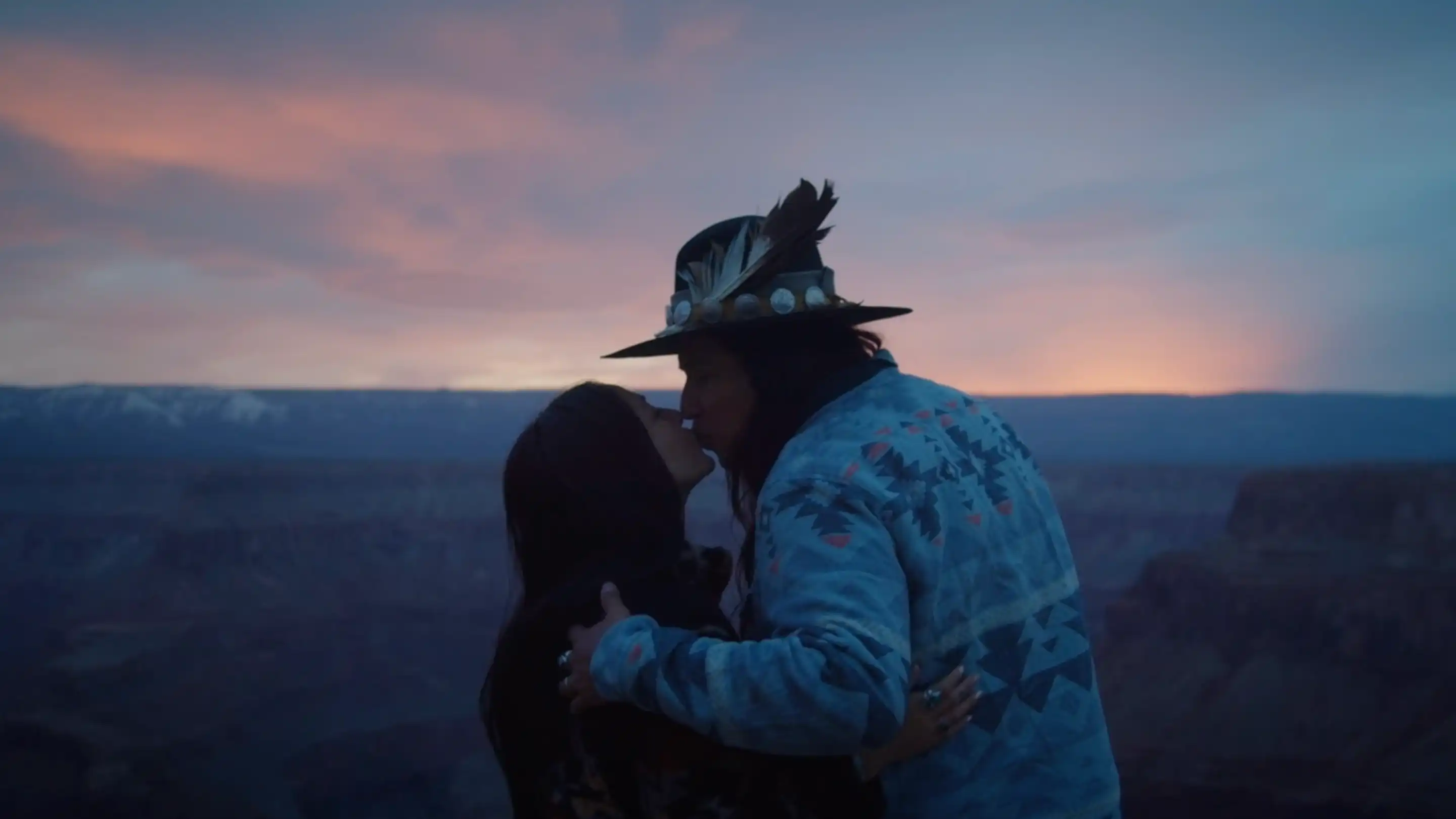 A couple kissing at sunset with a canyon landscape in the background.