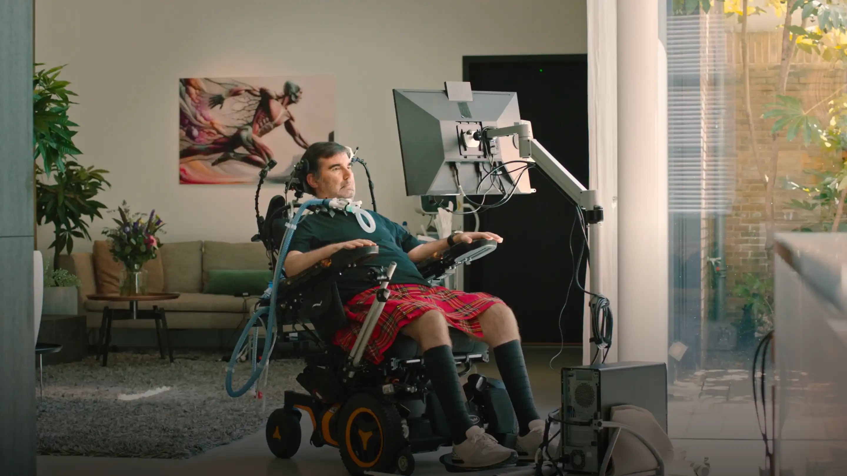 Person in a wheelchair using a computer with assistive technology in a living room.