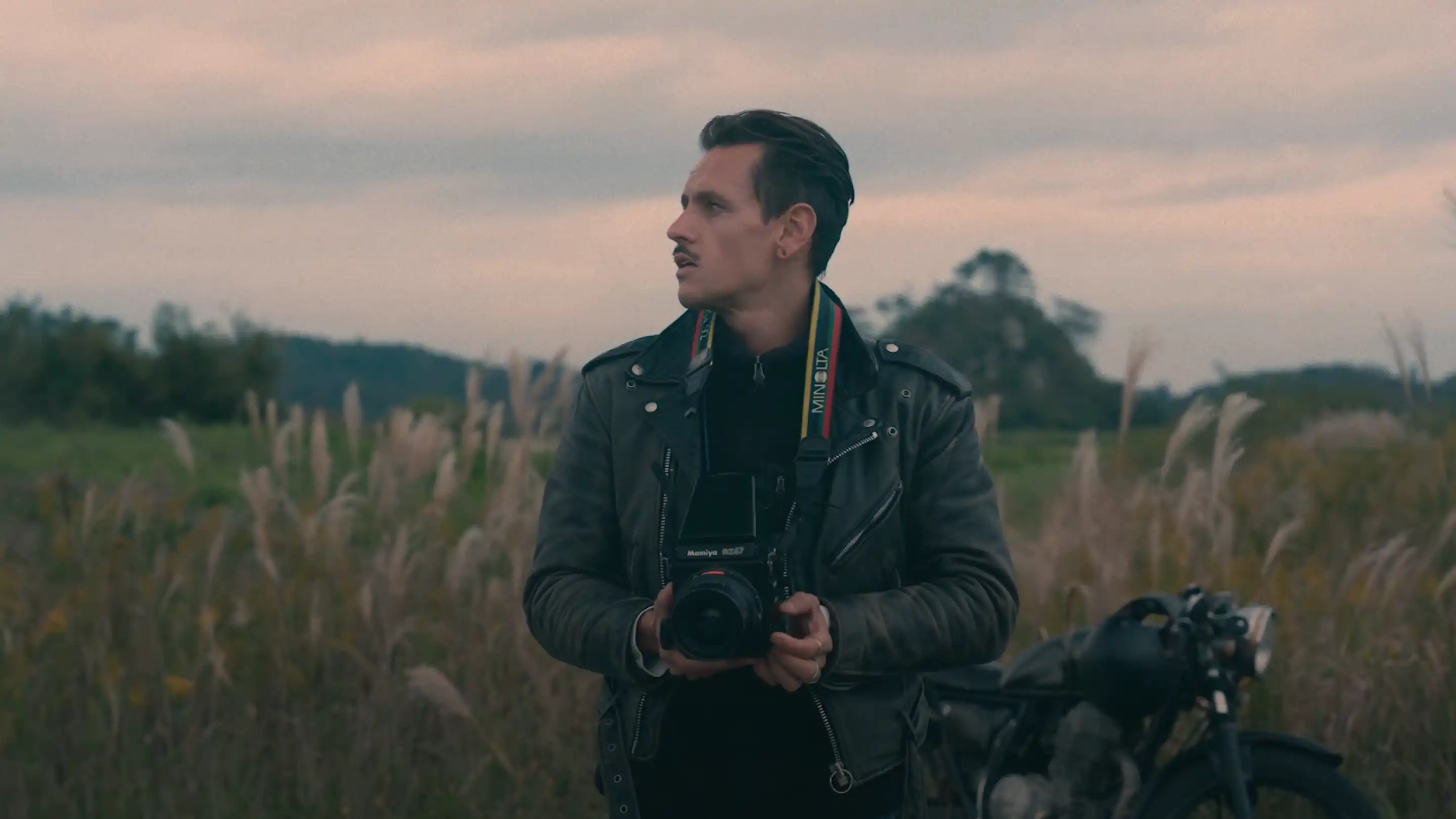 Man with a camera standing in a grassy field during sunset.