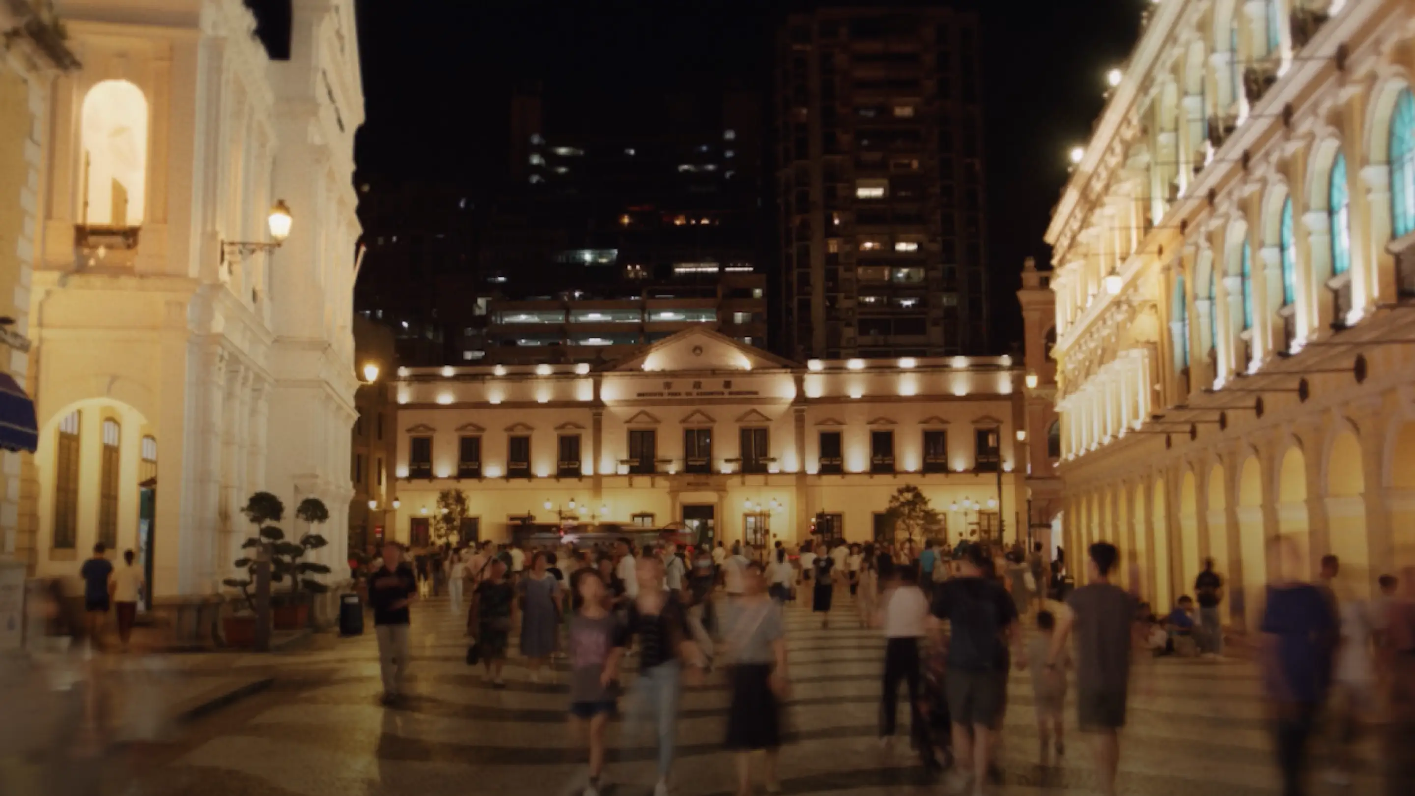 Crowd of people walking in front of illuminated historic buildings at night.