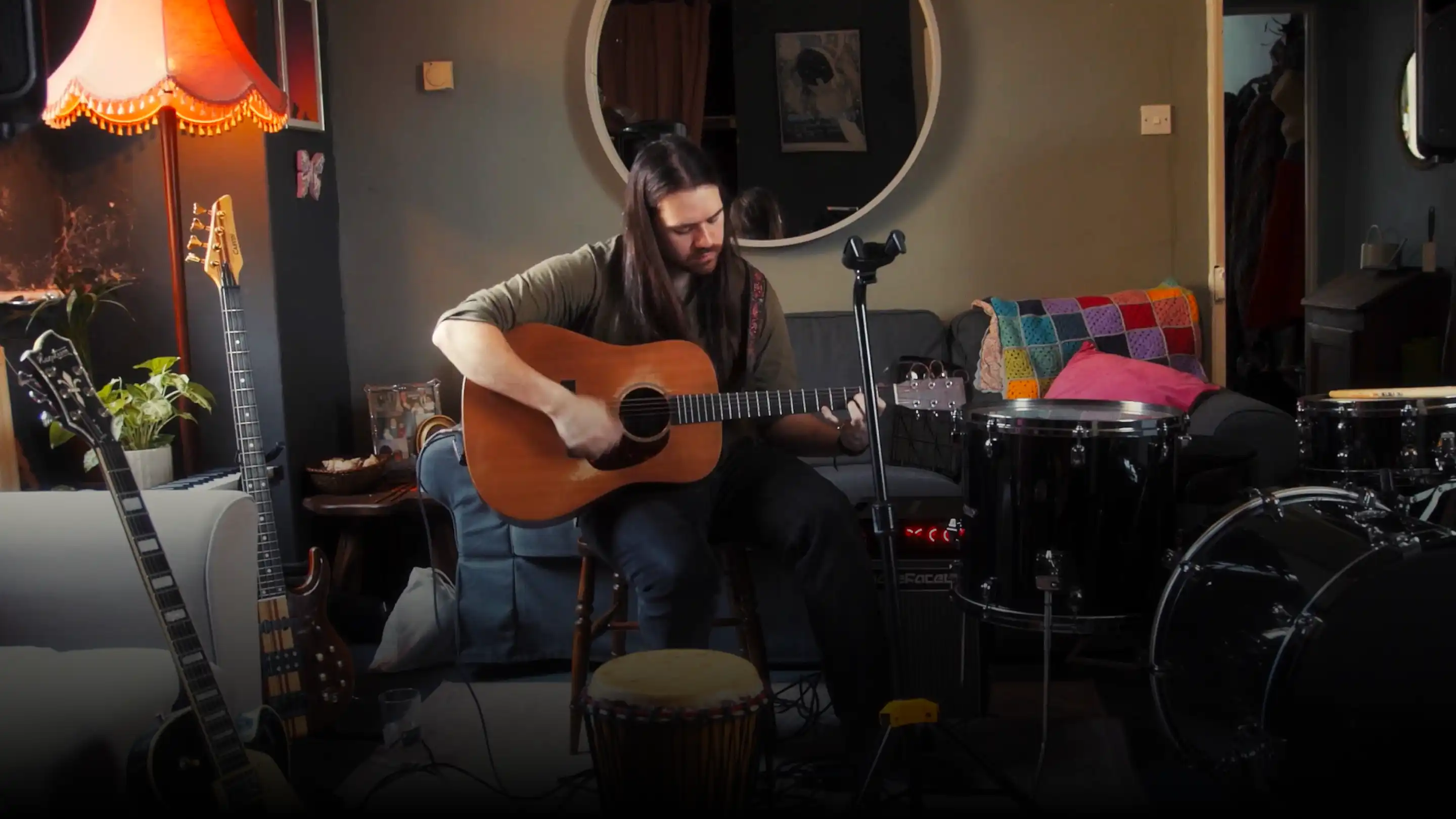 Man playing acoustic guitar in a cozy, decorated room with musical instruments.