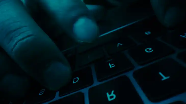 Close-up of hands typing on a backlit keyboard in low light.