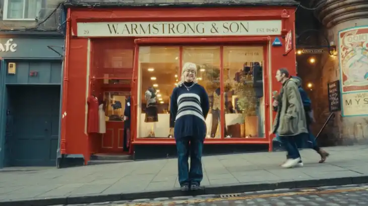 A smiling woman standing in front of W. Armstrong & Son clothing store on a city sidewalk.
