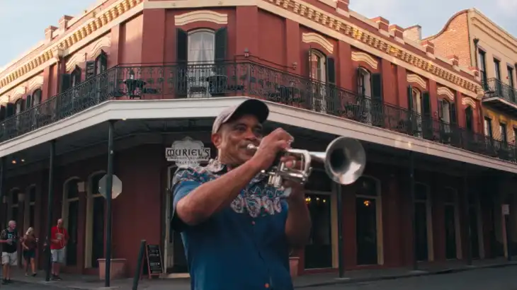 Man playing trumpet on street corner in front of a red brick building.