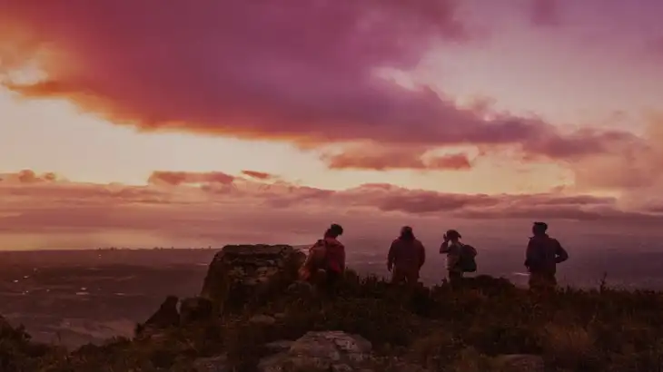 Four people standing on a hill during a colorful sunset sky.