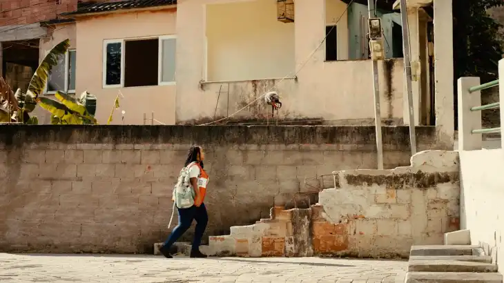 Woman walking up stairs next to a beige building with a concrete wall and stairs.