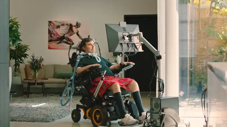 Person in a wheelchair using a computer with assistive technology in a living room.