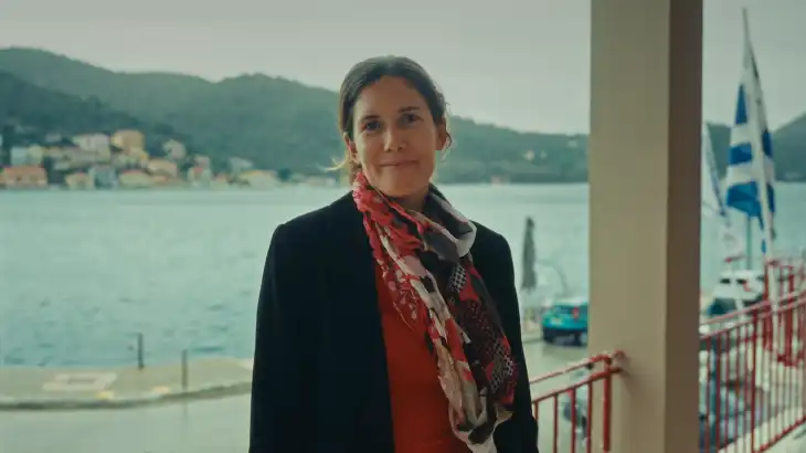 Woman standing by a waterfront with boats and hills in the background