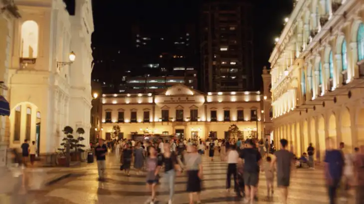 Crowd of people walking in front of illuminated historic buildings at night.