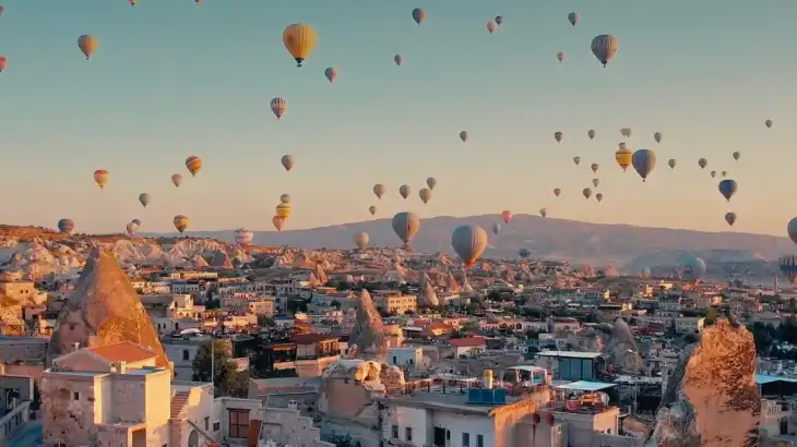 Numerous hot air balloons floating over a town with unique rock formations and cave houses.
